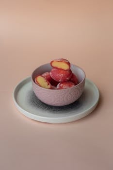 Frozen mochi spheres in a pink bowl on a pastel background create a minimalistic and vibrant food composition.