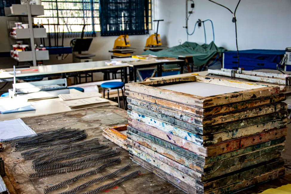 Cadres de sérigraphie en bois empilés dans un atelier textile, presses à chaud en arrière-plan