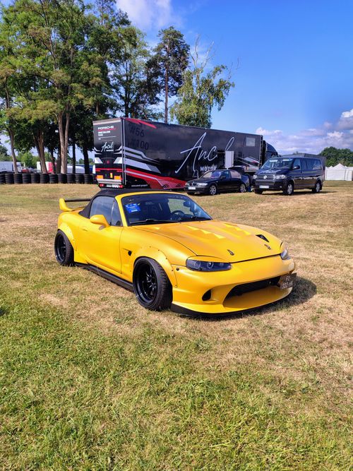 Free A striking yellow sports car displayed in an outdoor auto event with trees and vehicles in the background. Stock Photo