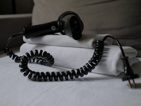 A coiled hair dryer placed on folded white towels, suggesting a hotel setting.