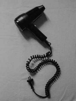 Minimalist black hair dryer with coiled cord on plain background.