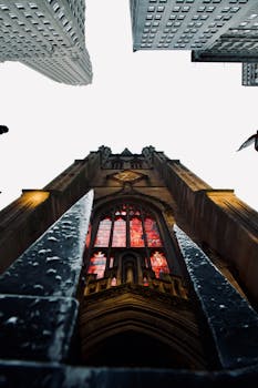 Dramatic angle of a Gothic church with stained glass windows surrounded by towering skyscrapers.