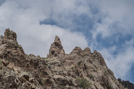 Rugged mountain peak under a cloudy blue sky showcasing geological formations outdoors.