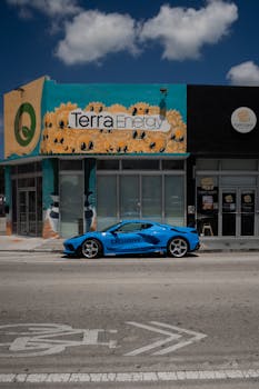 Striking blue sports car parked in front of colorful street mural under bright skies.