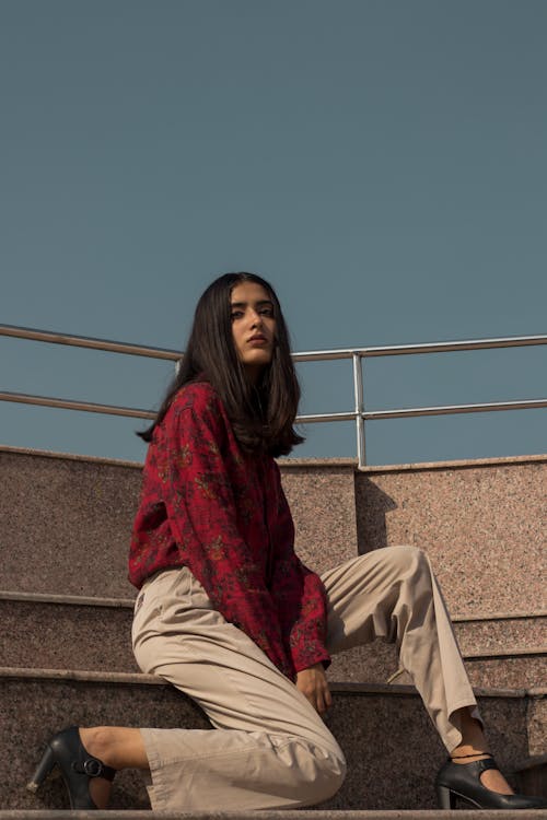 Woman in Red Long-sleeved Top and Brown Pants Sitting on Stair