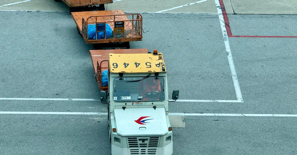 A tow tractor pulls cargo containers on an airport tarmac, showcasing aviation logistics.