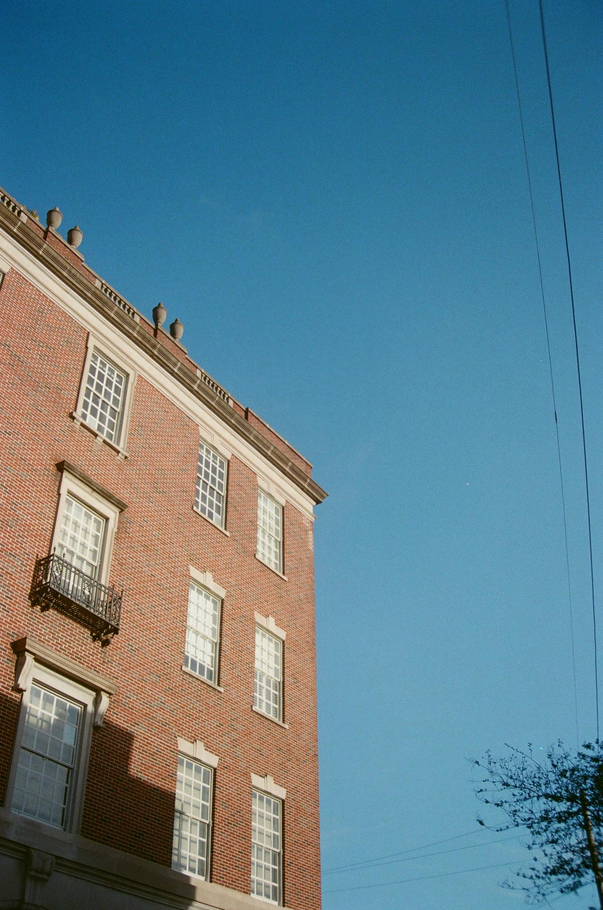 Gratuit Fotografie a unei clădiri din cărămidă roșie cu ferestre pe fundalul unui cer albastru senin, surprinsă în timpul zilei. Fotografie de stoc