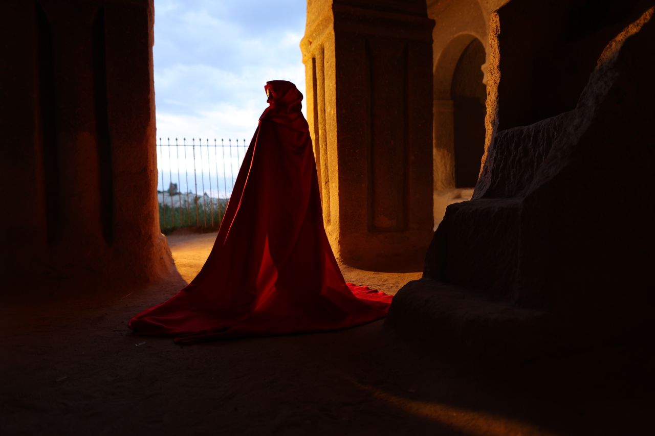 a cloaked figure in red silhouetted against the light from an ancient