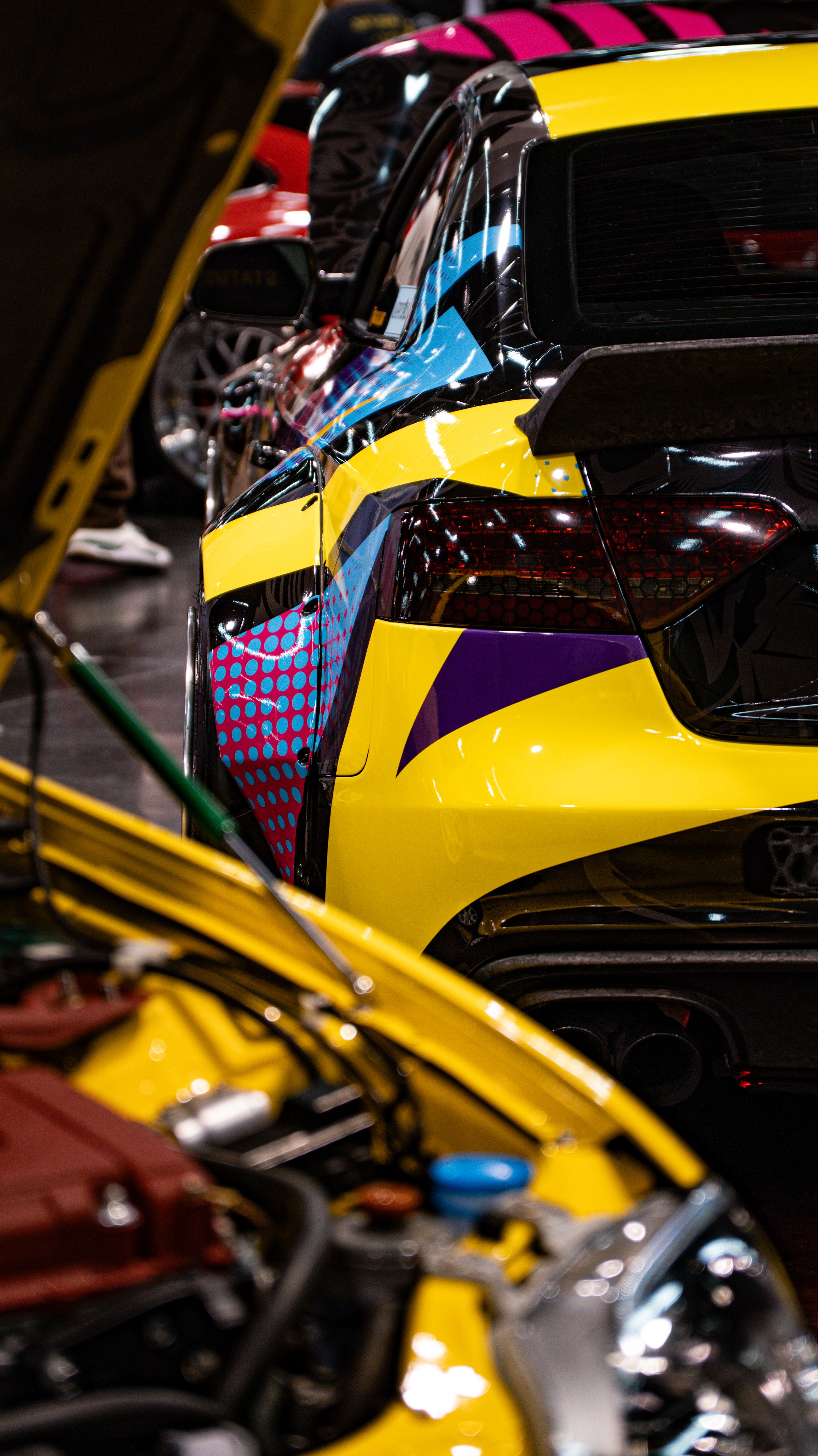 Close-up of colorful custom cars with unique designs at an indoor auto show event.