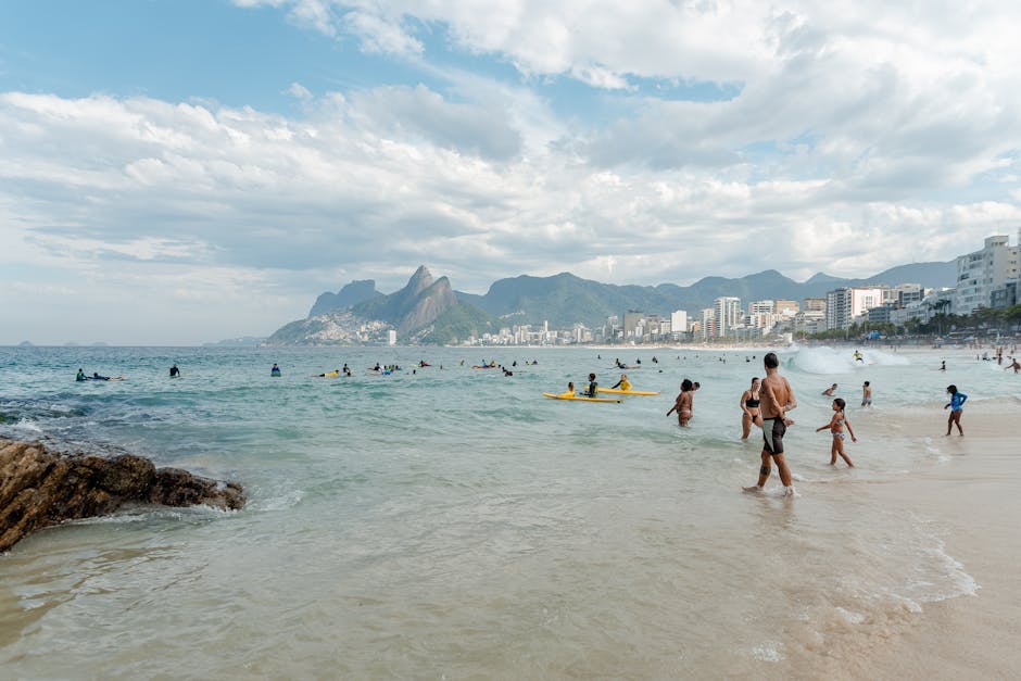 People enjoying a sunny day at Ipanema Beach in Rio de Janeiro with surf and cityscape views.
