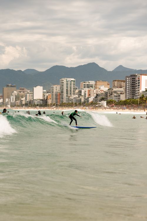 Free A surfer enjoying the waves at Ipanema Beach with Rio de Janeiro's skyline in the background. Stock Photo