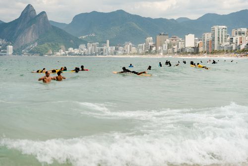 Free Surfers paddling in the ocean at Ipanema Beach, Rio de Janeiro, with mountains in the background. Stock Photo