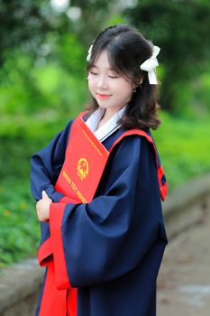 Young woman smiling in a graduation gown with a diploma outdoors, celebrating her academic achievement.