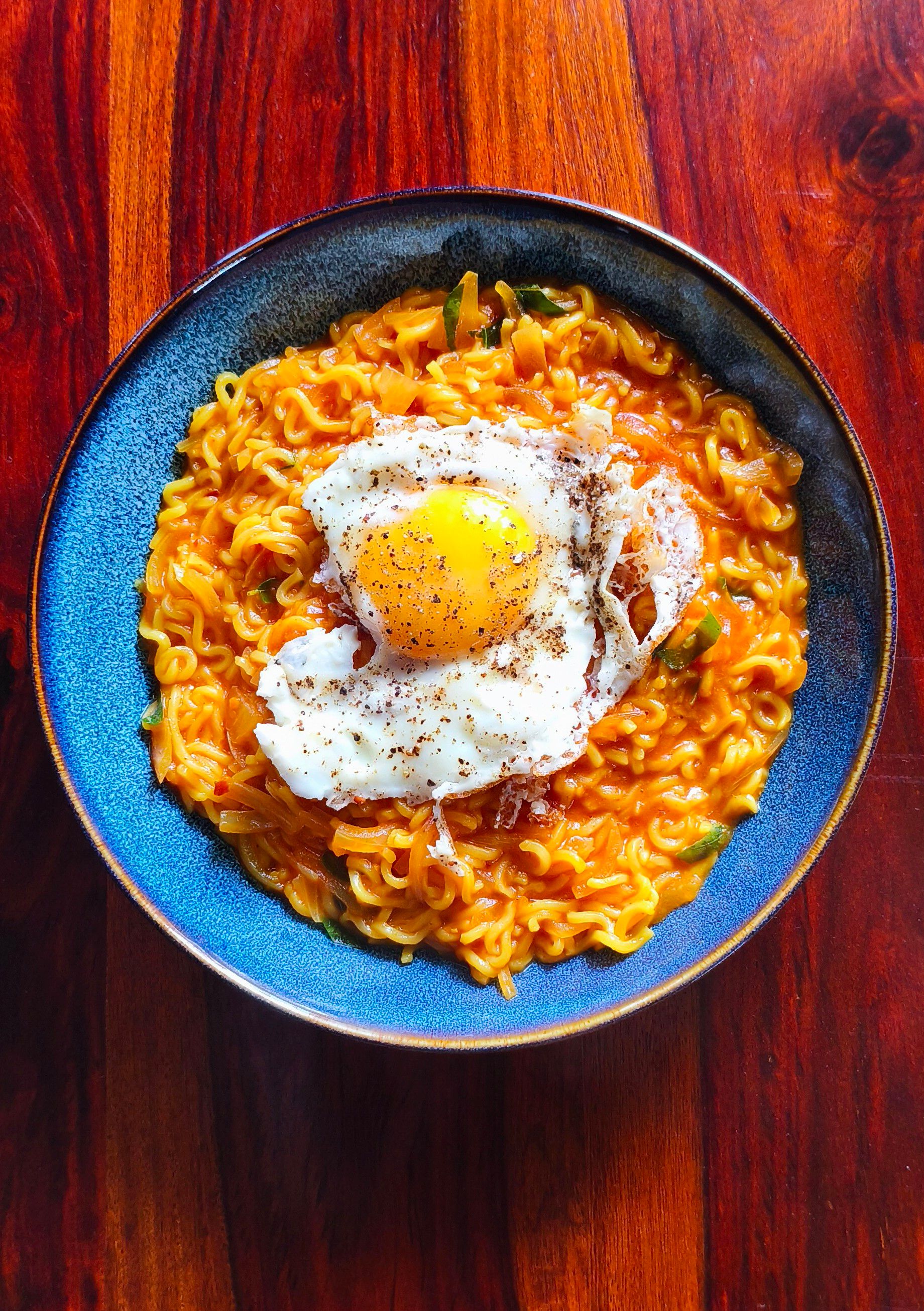 A mouth-watering bowl of spicy ramen topped with a sunny-side-up egg on a wooden table.