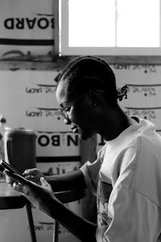 Side profile of a young man engrossed in his smartphone, indoors in Abuja, Nigeria.
