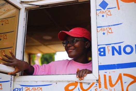A woman in a red cap and glasses smiles through a window in Abuja, Nigeria.