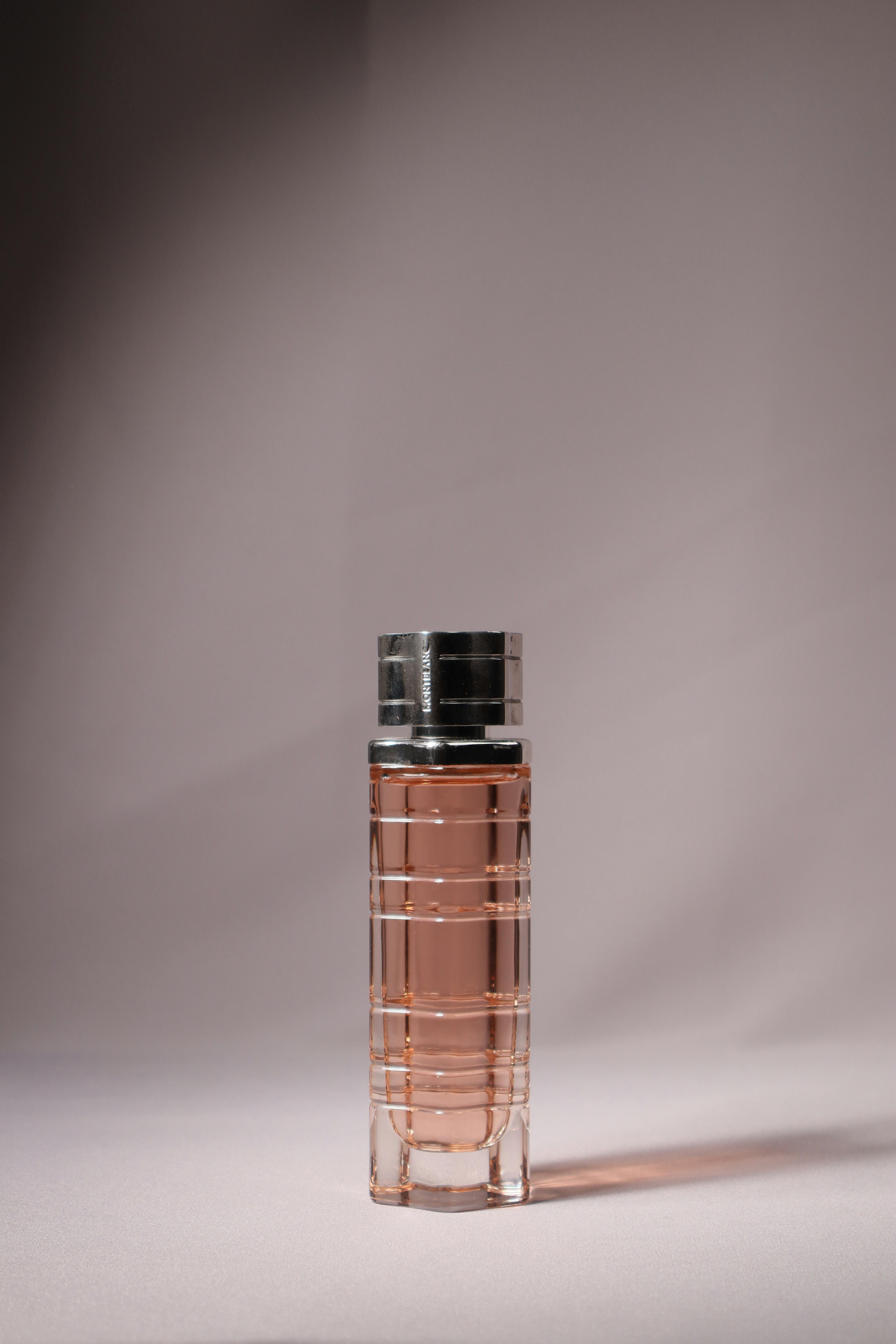 Sleek glass perfume bottle with pink liquid displayed against a neutral backdrop.