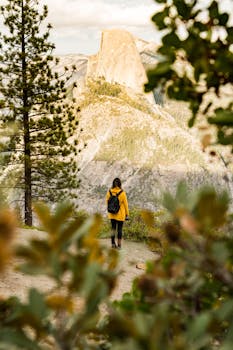 在加州约塞米蒂国家公园，一位穿着黄色夹克的徒步旅行者正在欣赏半圆顶令人惊叹的秋景