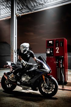 Motorcycle rider refueling at a gas station under a night sky.