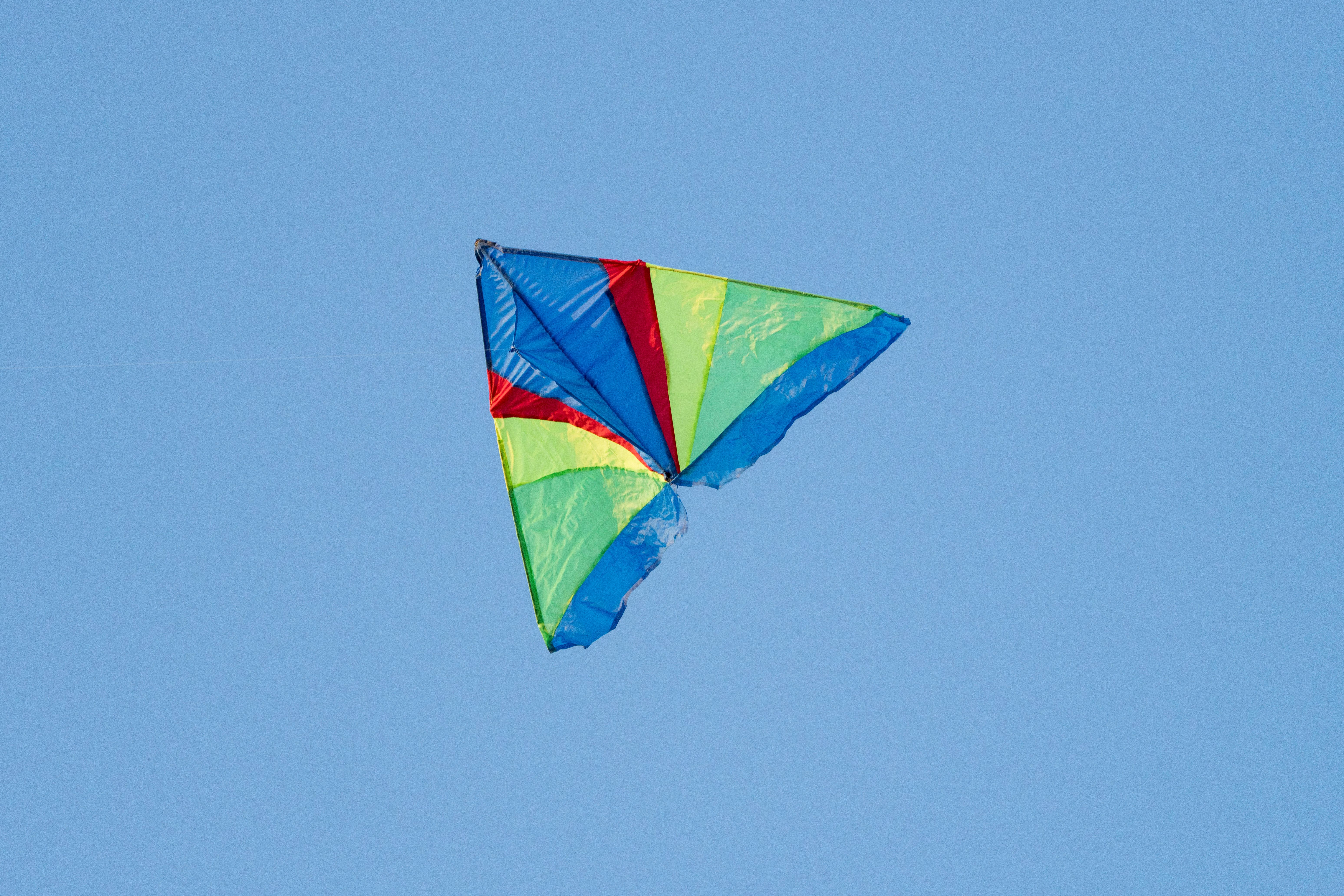 A vibrant multi-colored kite flying high against a clear blue sky, capturing a sense of freedom and joy.