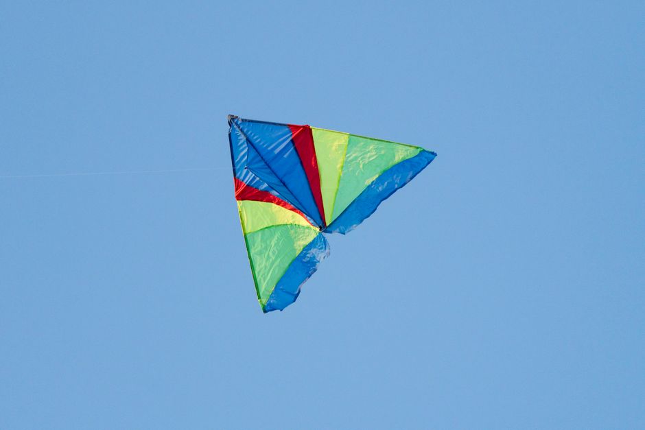 A vibrant multi-colored kite flying high against a clear blue sky, capturing a sense of freedom and joy.