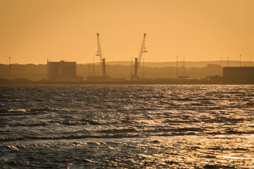 Free Industrial harbor with cranes silhouetted against a golden sunset, reflecting on the water. Stock Photo