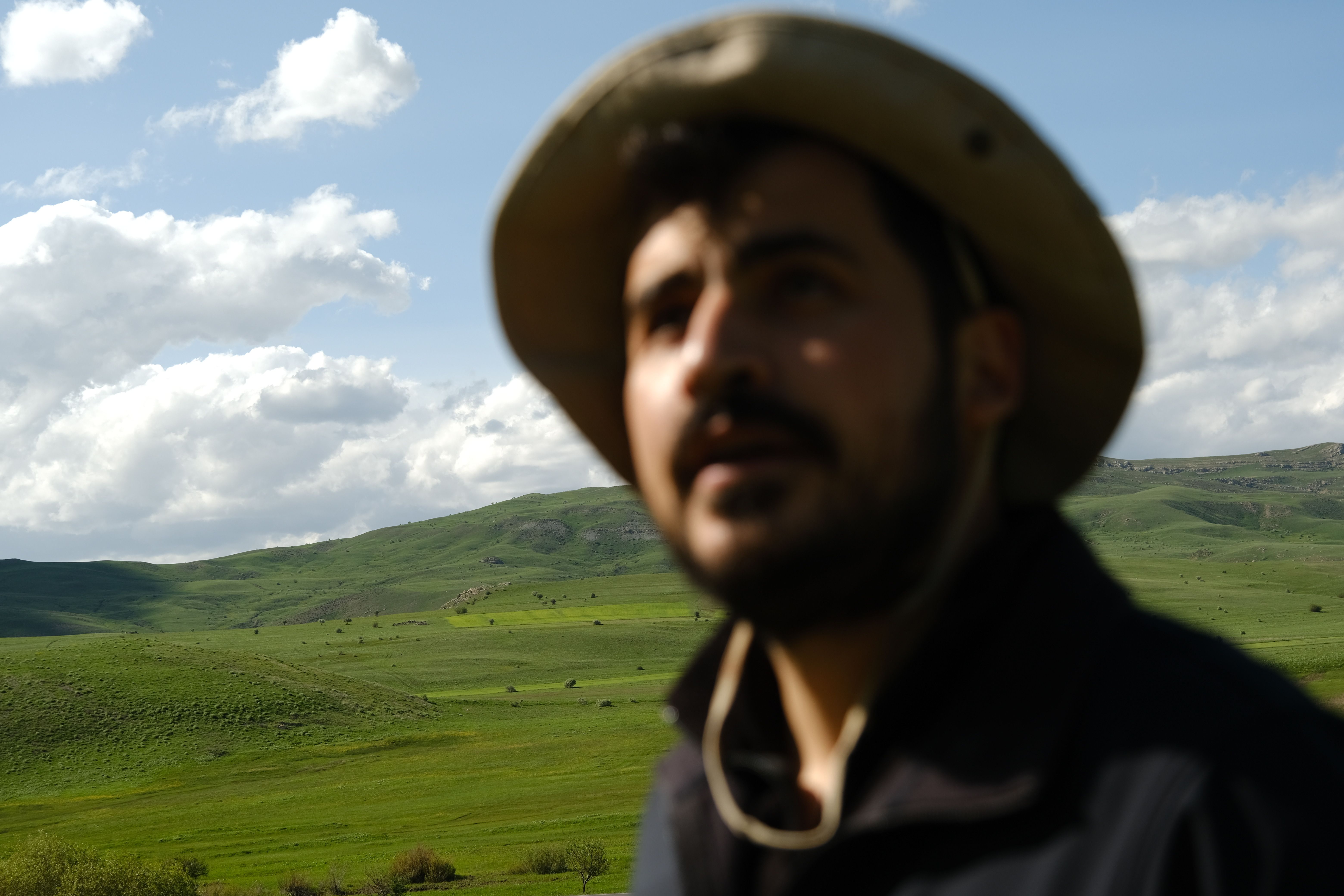 A man in a hat gazes at the lush green hills under a cloudy sky.