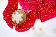特写镜头中，冬季雪地里一只红色手套拿着热饮和雪花棉花糖