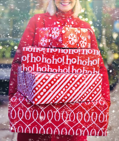 Free A woman joyfully holding a stack of red Christmas presents in a snowy outdoor setting. Stock Photo