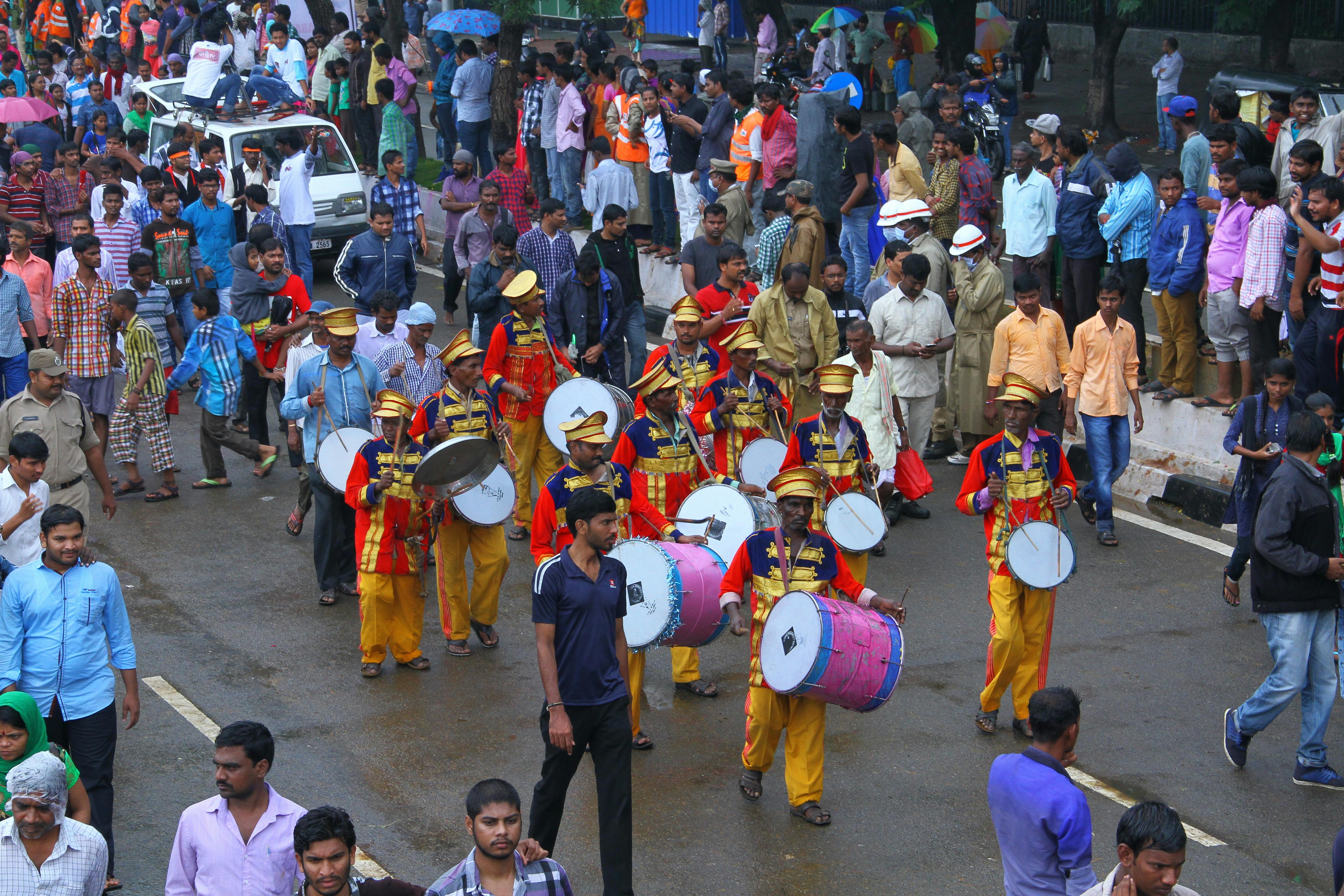 Lively parade showcasing musicians in colorful attire drawing a large crowd of spectators on a rainy day.