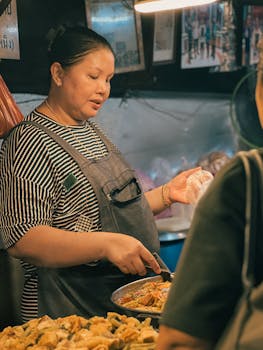A street food vendor prepares a dish at a bustling night market. Authentic cultural experience.