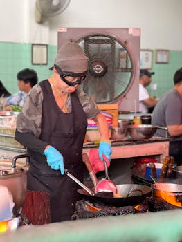 Street food chef cooks with wok in an indoor kitchen, creating a vibrant culinary scene.