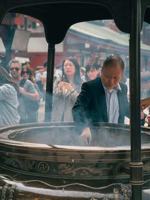 Free A man immersed in ritual at a traditional incense burner amidst a bustling temple courtyard. Stock Photo