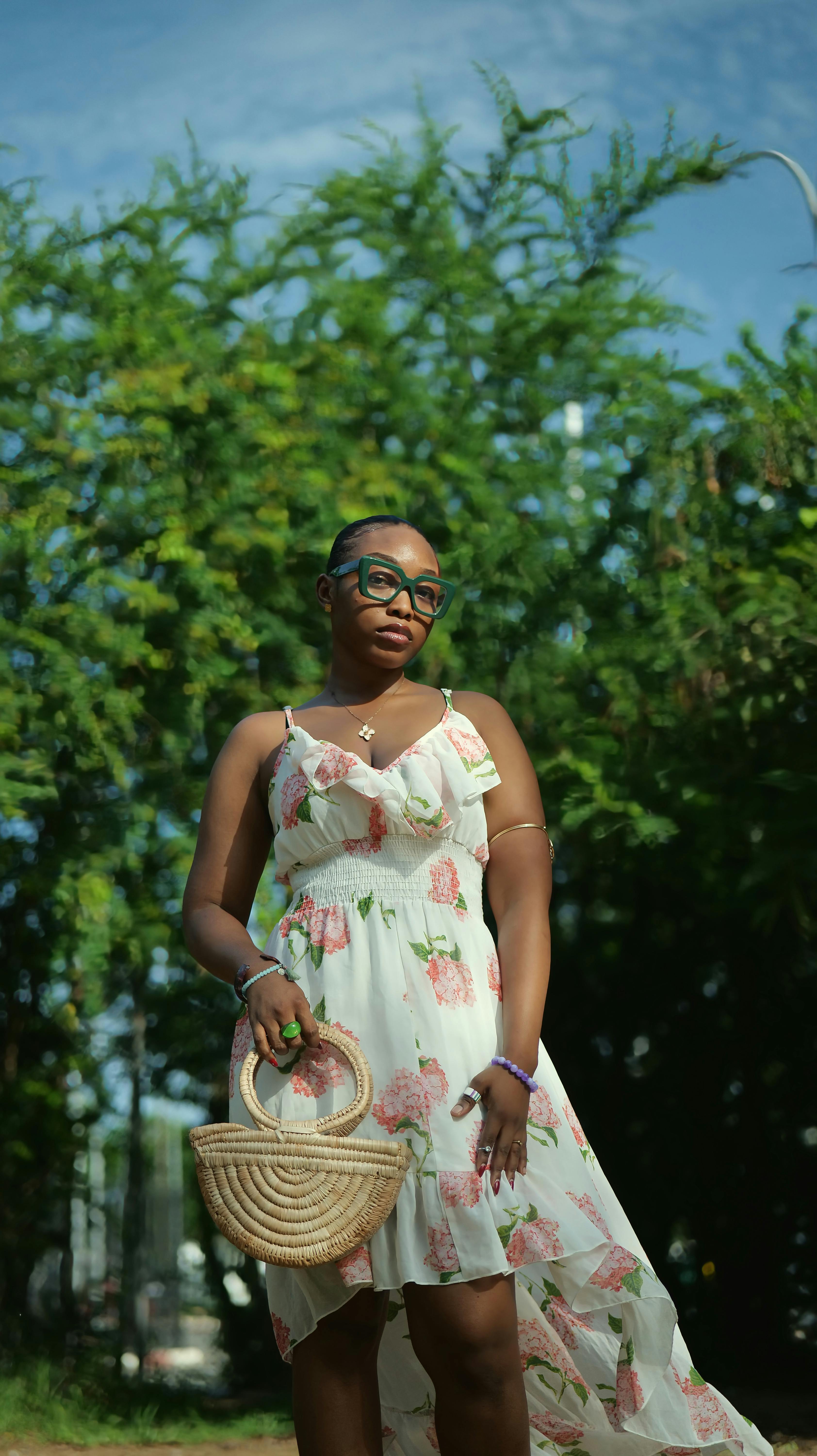 Woman in floral dress posing confidently in sunny outdoor setting.