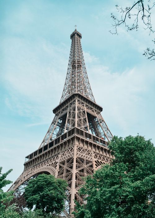 Free Eiffel Tower reaching into the sky, surrounded by green trees in Paris, France. Stock Photo