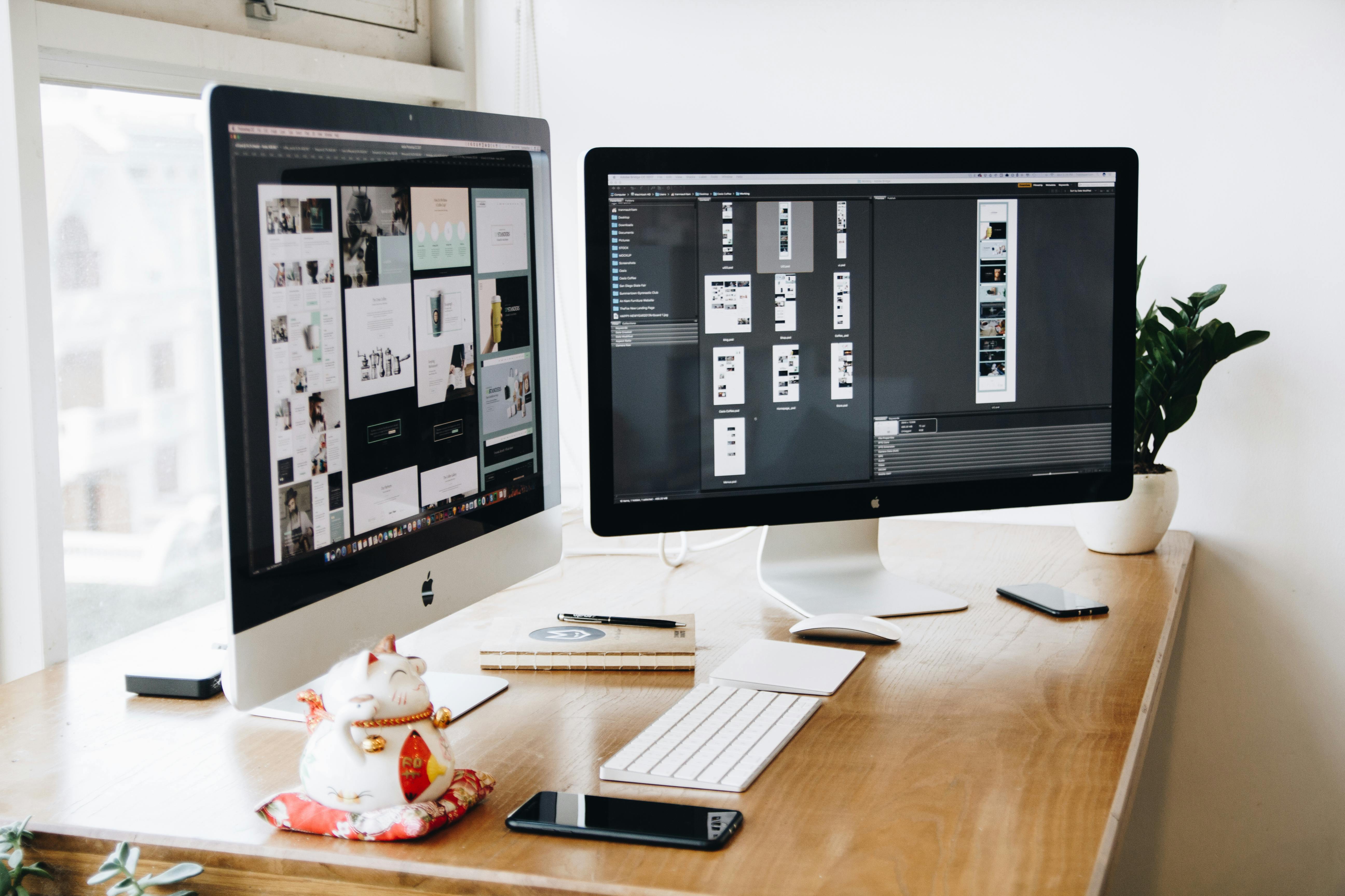 two imac s with keyboard and phones on desk