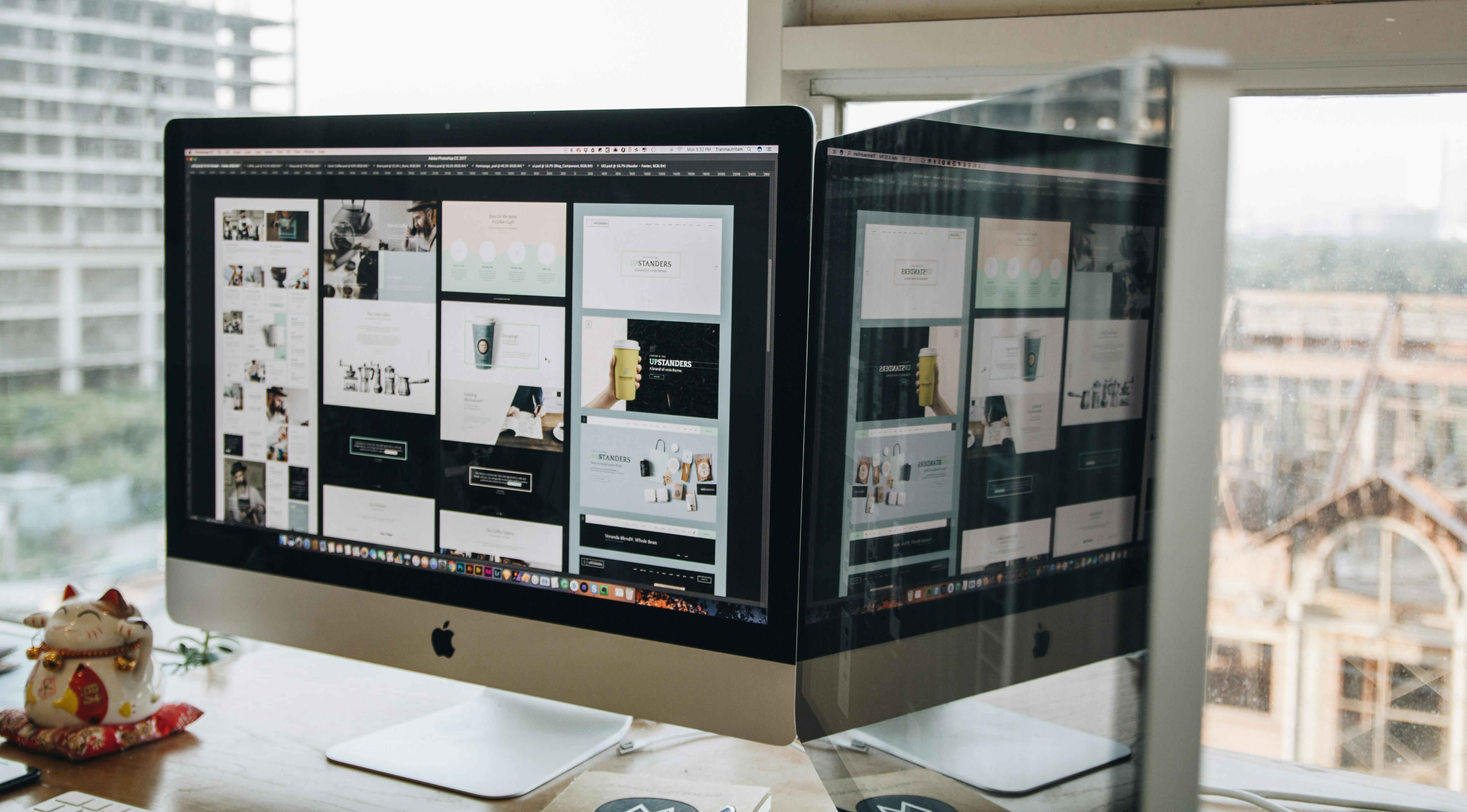 Dual monitors on a desk, showcasing web design in a modern office setting.