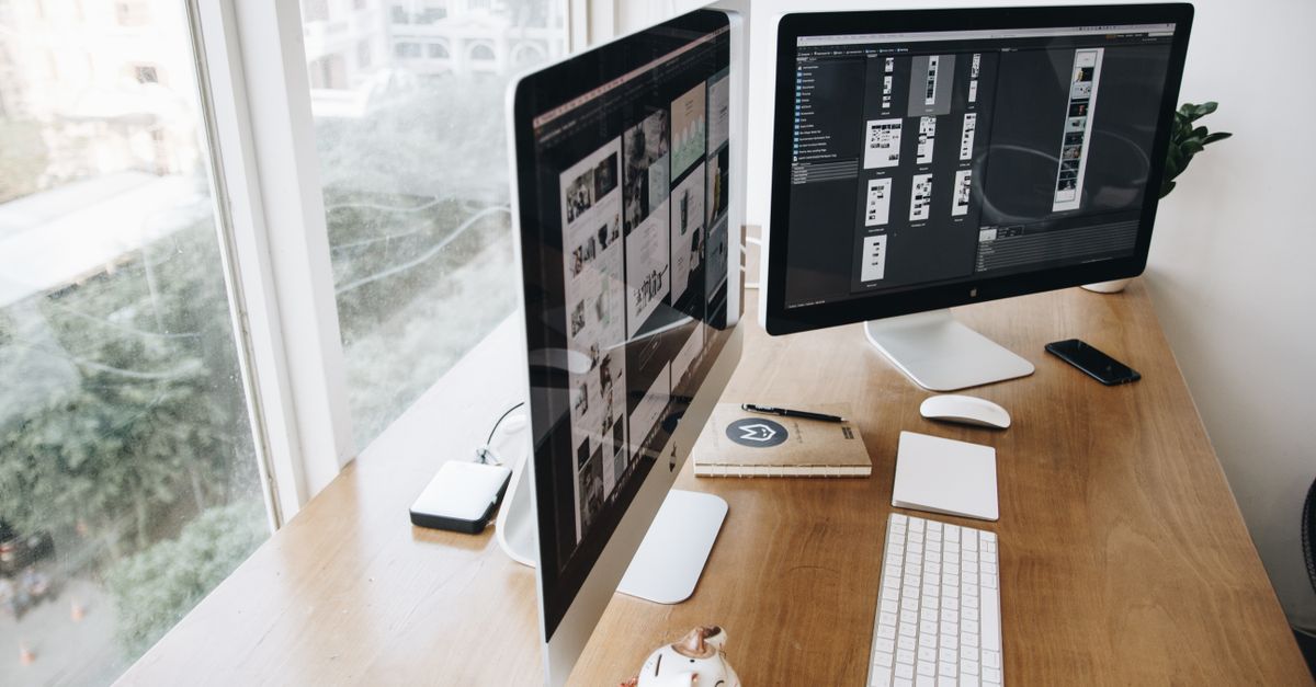 A well-organized modern office desk with dual computer screens and various devices.