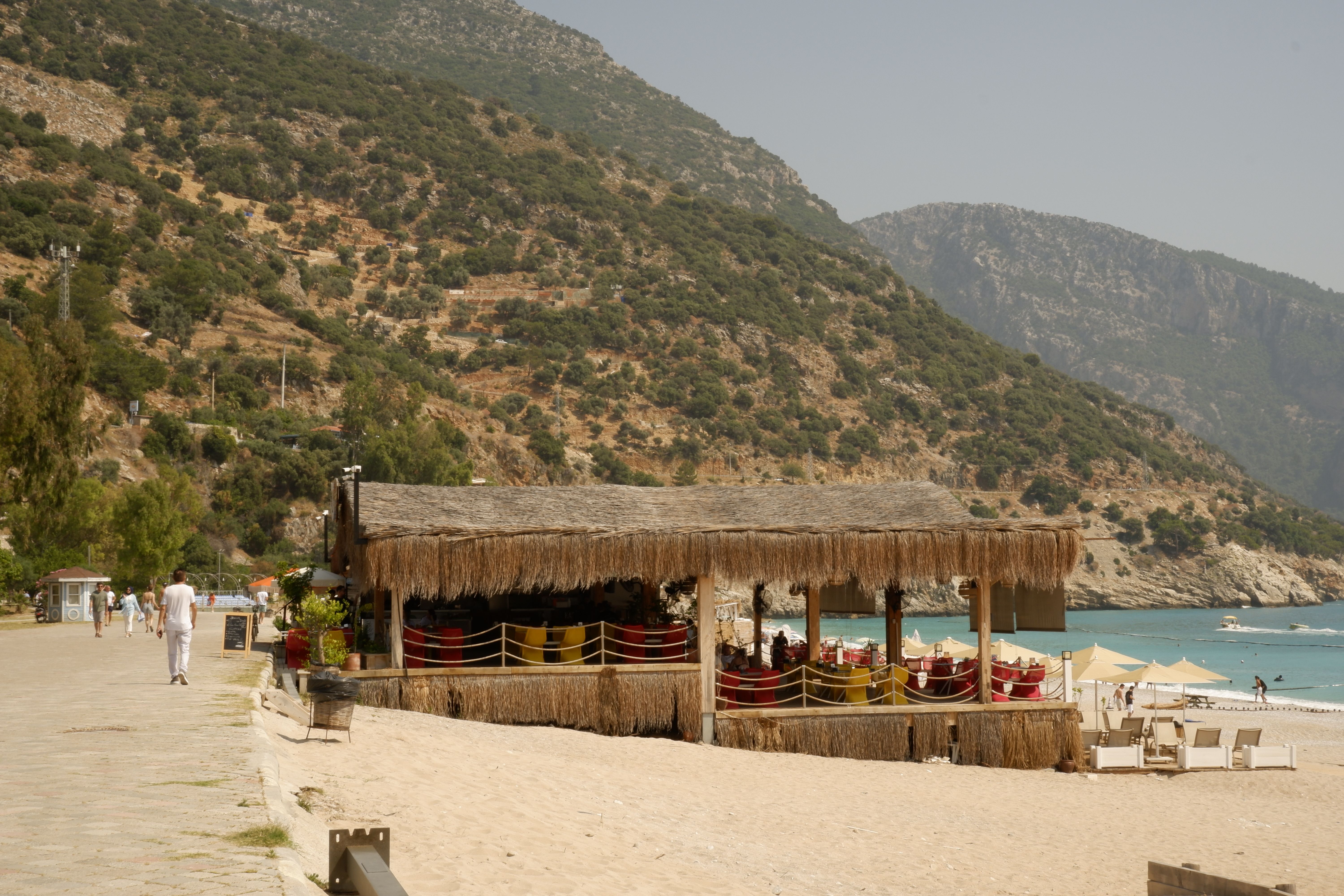 solo traveler working on laptop at a quiet beachside café with turquoise water in the background