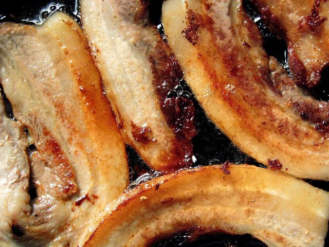 Golden-brown crispy bacon strips sizzling in a frying pan, perfect for breakfast settings.
