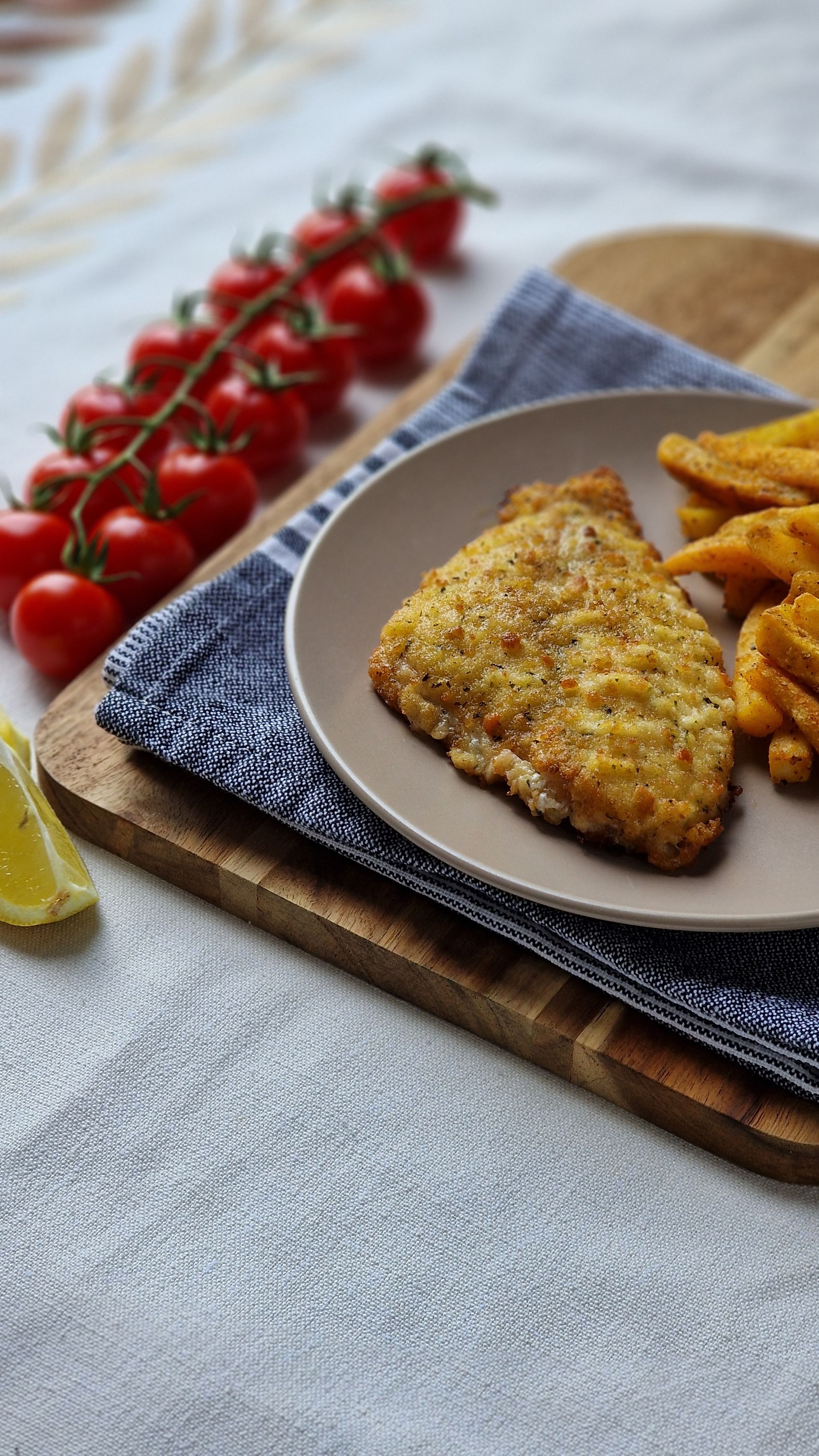 Golden-brown cornmeal-crusted fish fillets stacked on a wire rack with lemon wedges and hot sauce on the side.