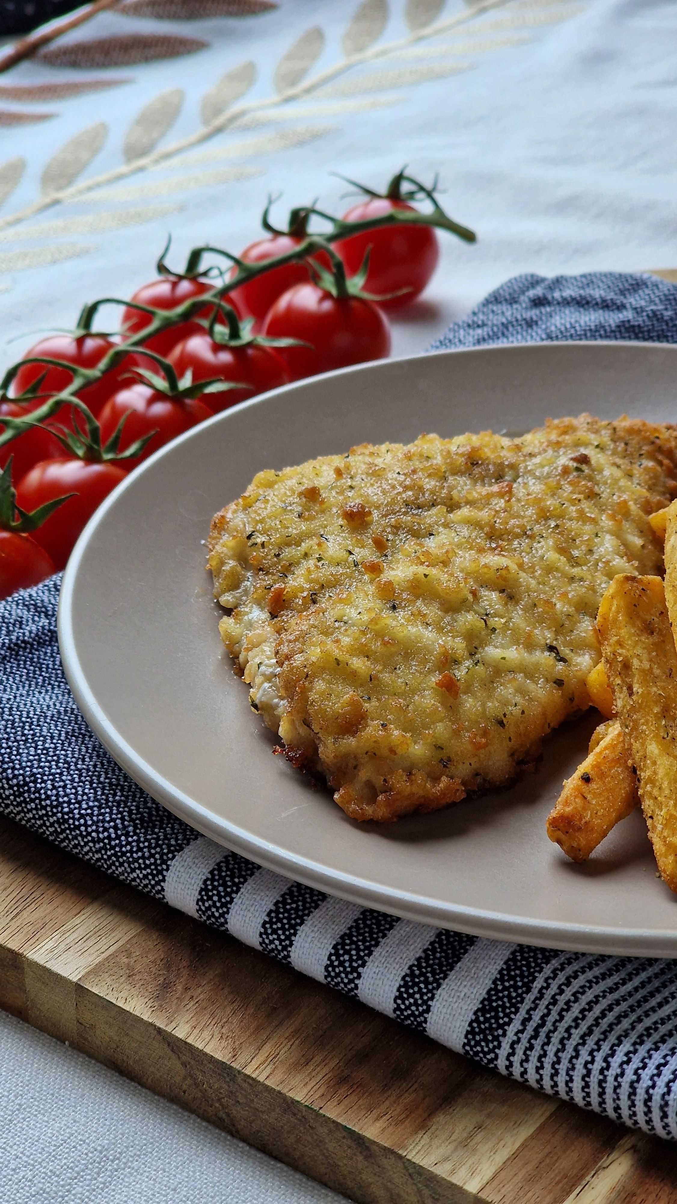 Fotomural Sabroso escalope empanizado con patatas fritas crujientes y tomates cherry frescos sobre una mesa de madera.