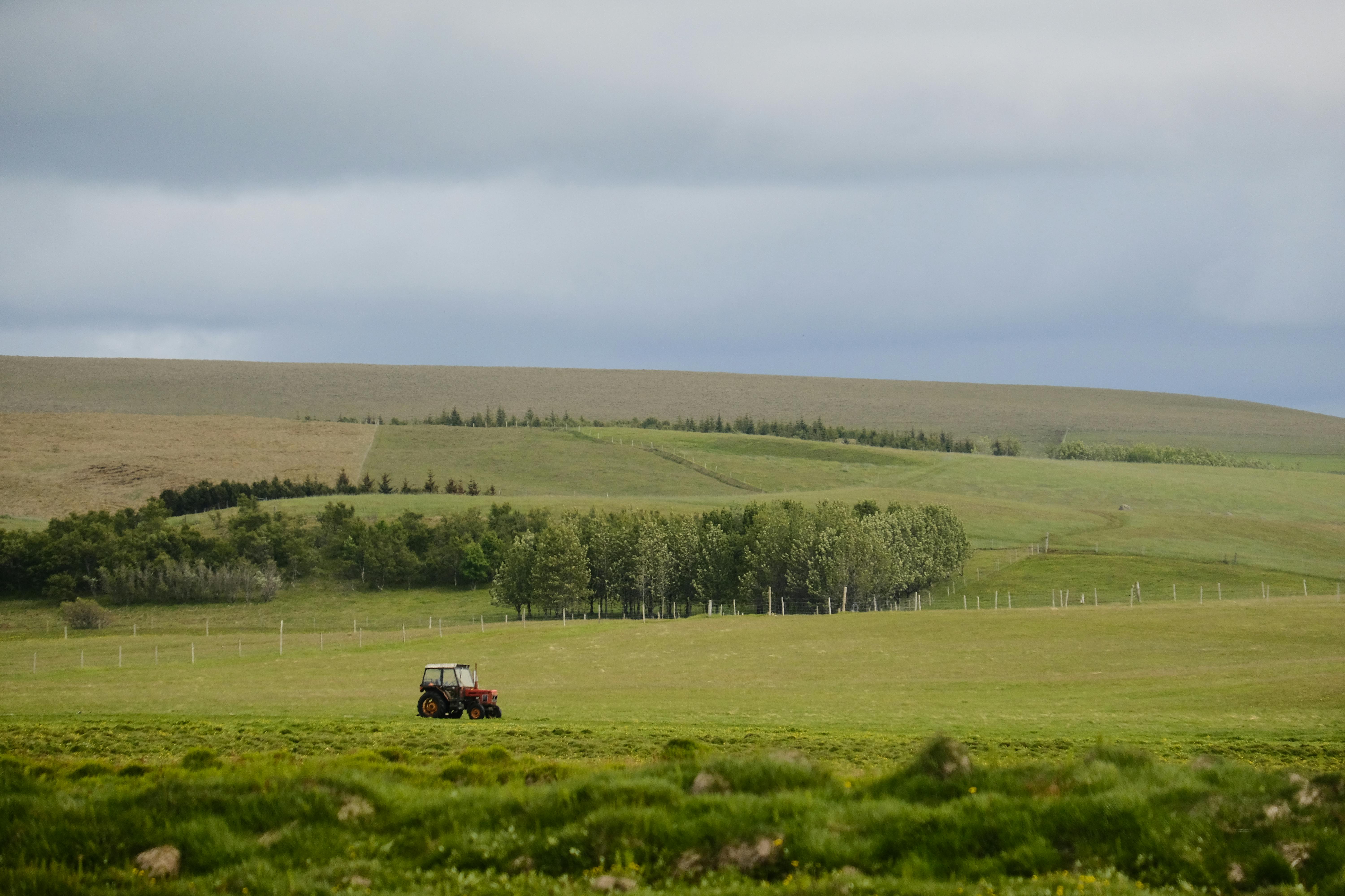 A peaceful rural scene featuring a lone red tractor on expansive green fields under a cloudy sky.