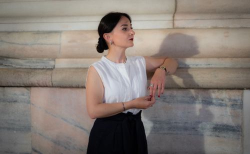 Free Stylish woman depicted in an elegant pose against a classic marble wall in Milan, Italy. Stock Photo