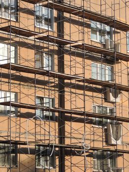 Urban building facade with scaffolding under construction, sunlight casting shadows.