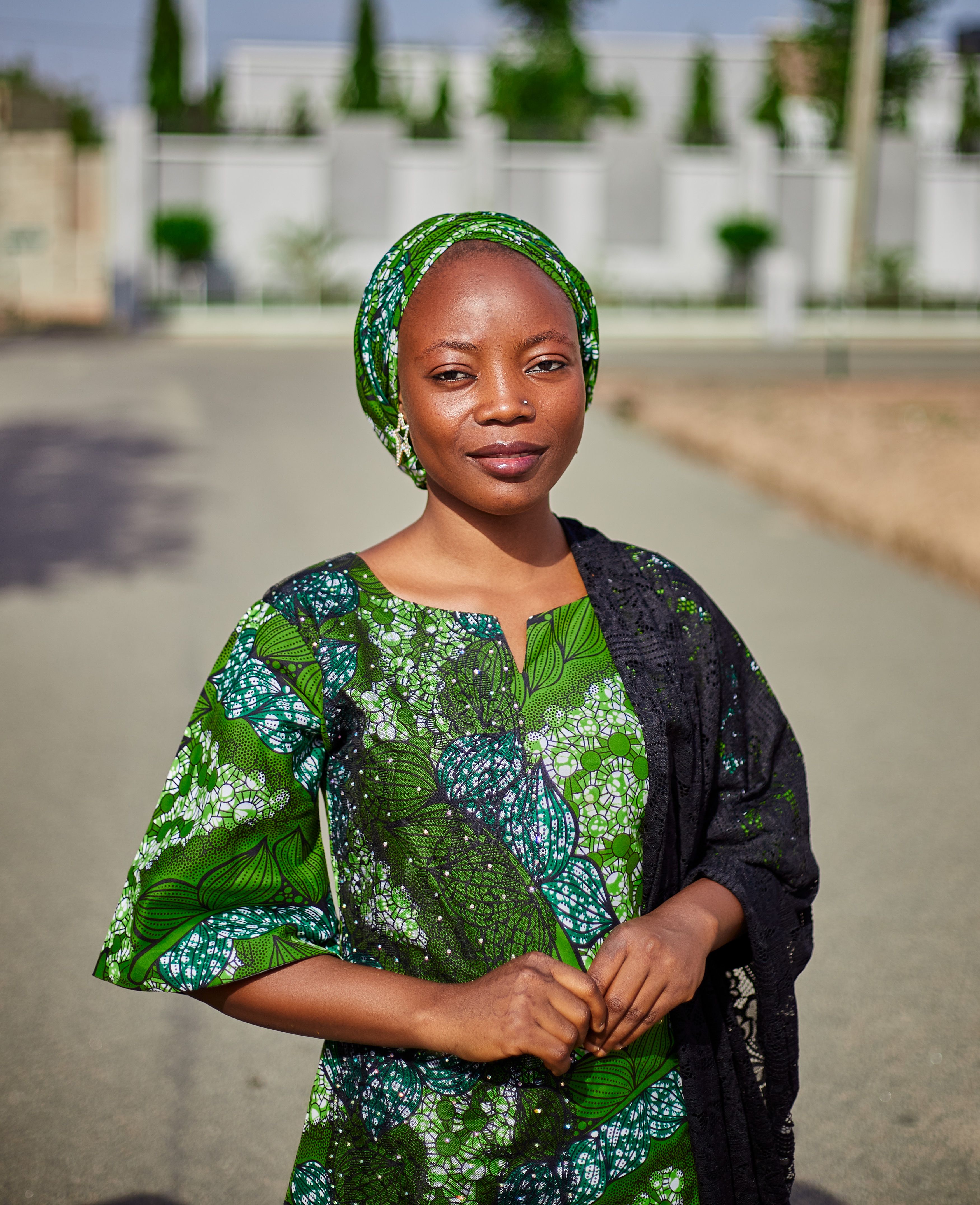 A confident woman in vibrant green traditional attire stands outdoors on a sunny day.