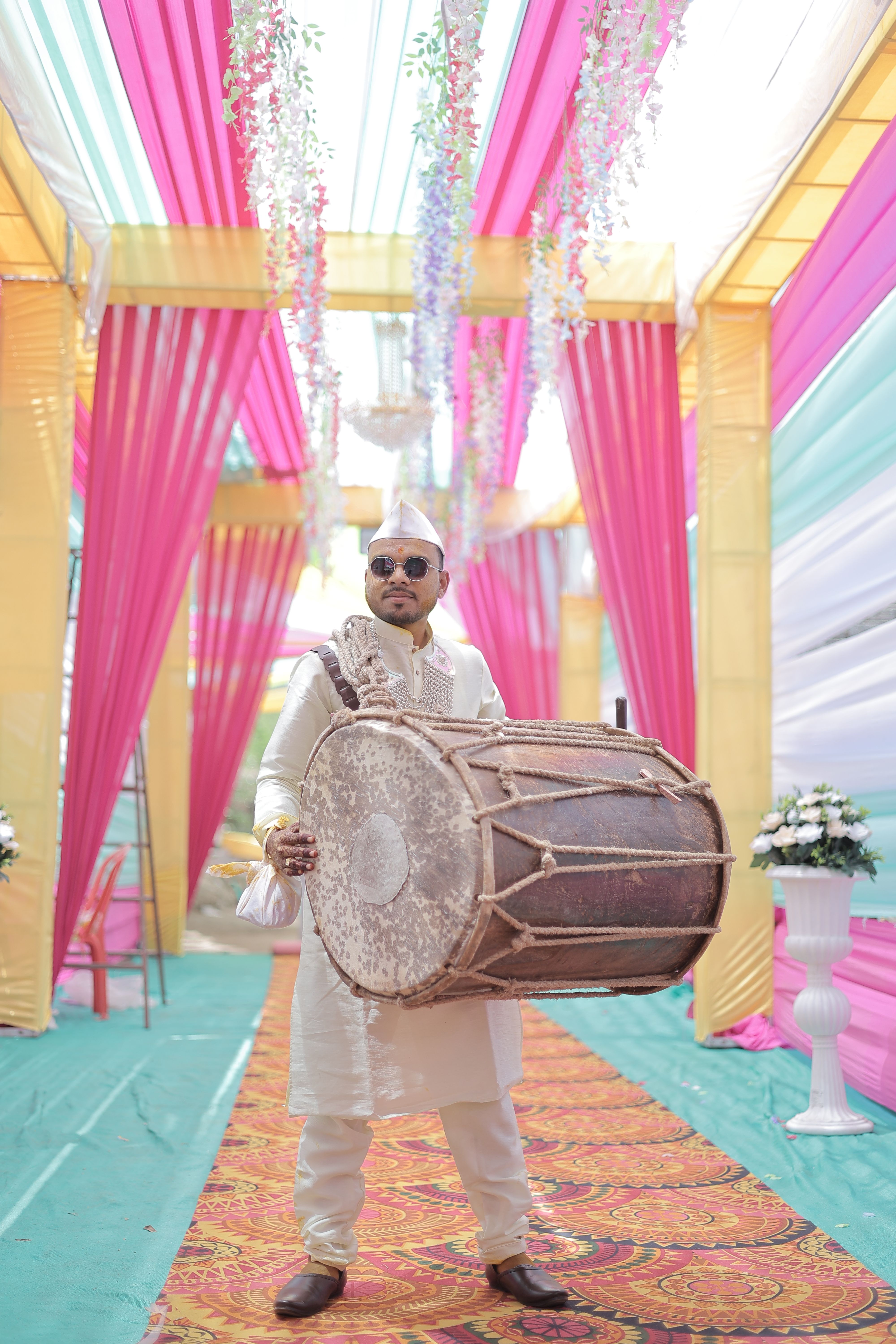 Musician in traditional attire playing drum at vibrant Indian wedding event.