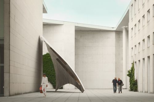 Free Urban scene with modern architecture and a large, unique sculpture, featuring people walking. Stock Photo