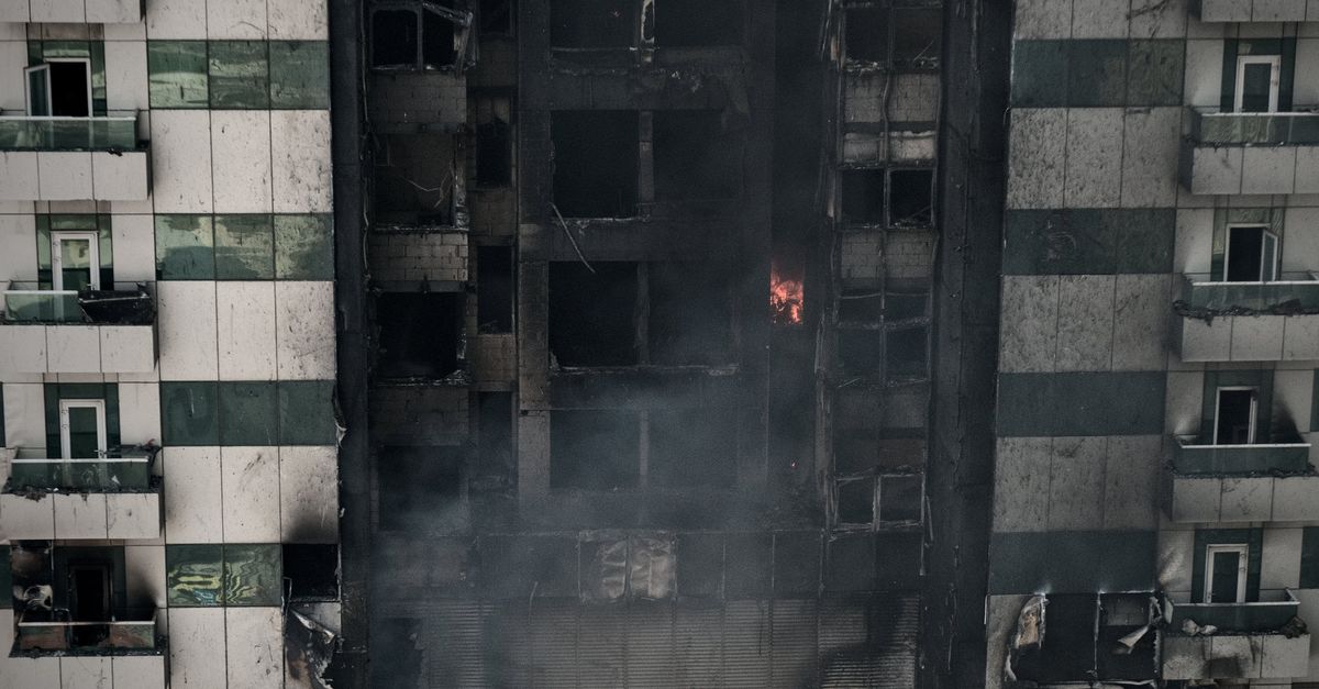 A high-rise building's facade shows severe fire damage with lingering smoke.