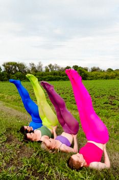 Four people doing colorful yoga poses in an open field, vibrant leggings stand out.
